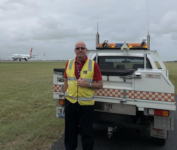 Airport worker in vest near service vehicle and airplane